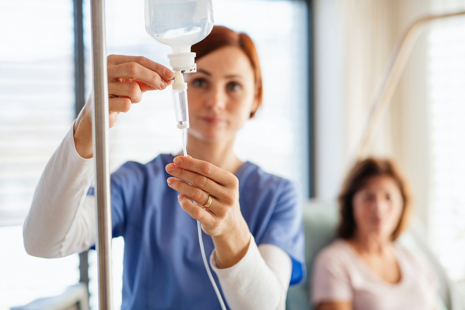 A nurse with IV drip and patient in bed in hospital room.